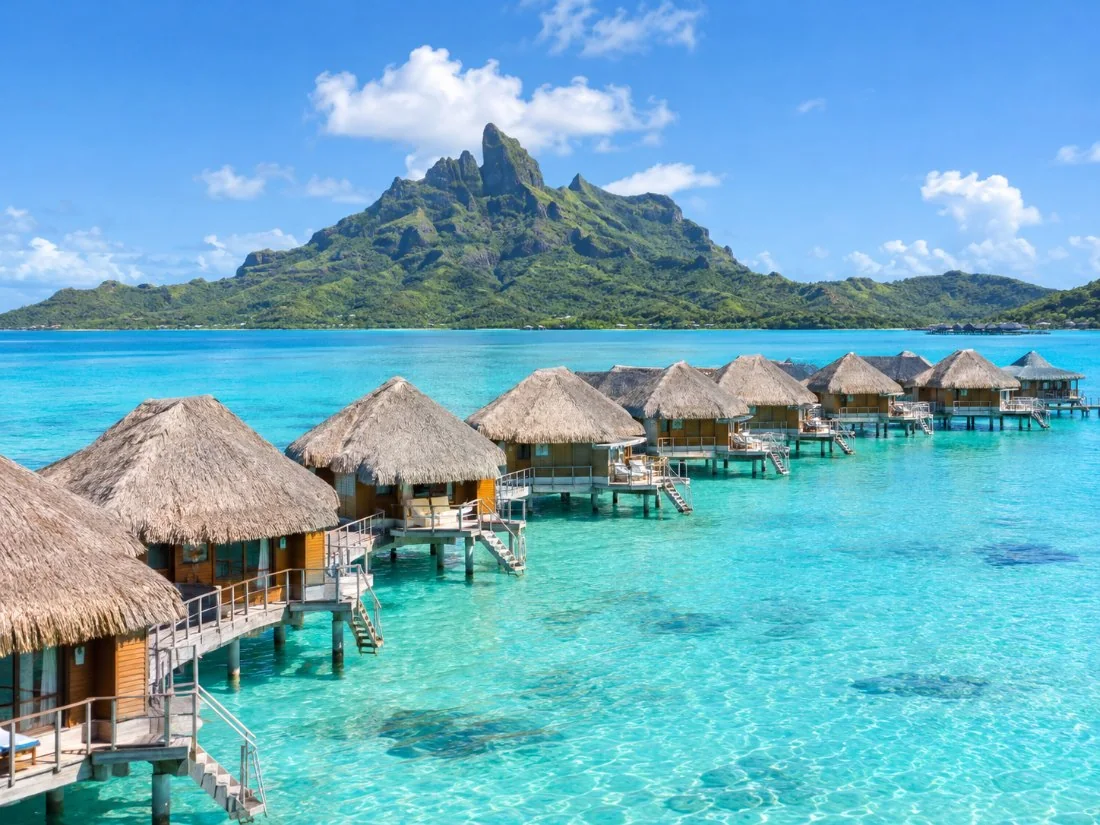 Eine Reihe von Überwasser-Bungalows auf Pfählen über dem helltürkisfarbenen Wasser der Bora-Bora-Lagune