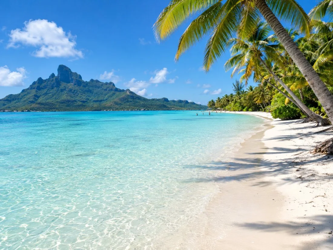 Der lange weiße Sandstrand von Matira mit Palmen und flachem türkisfarbenem Wasser